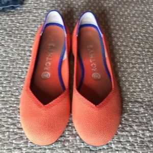 Orange Rothy’s with Blue/White stripe on heel.